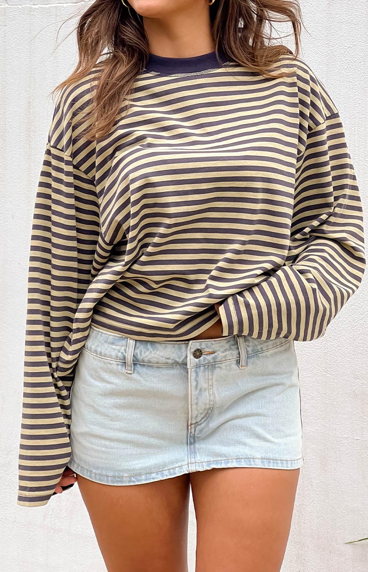 brunette girl wearing a light wash denim mini skort paired with an oversized navy and beige striped long sleeve shirt