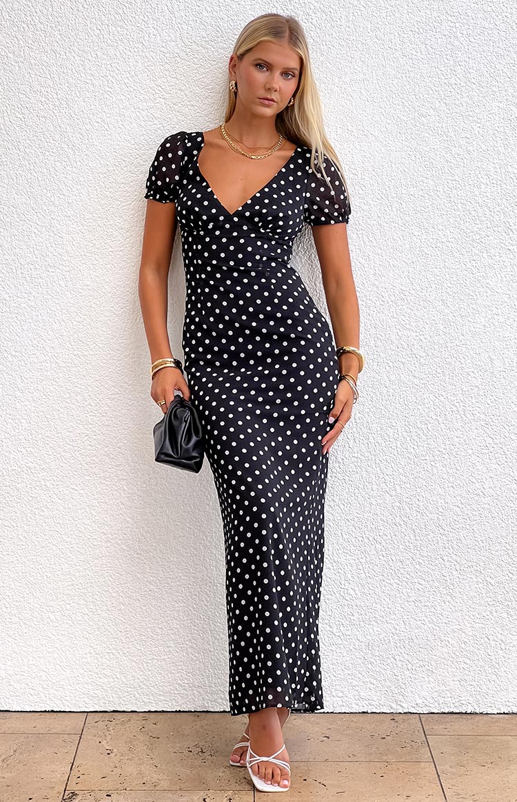 Blonde model wearing a black polka dot maxi dress with short puff sleeves and a v neckline paired with gold jewellery
