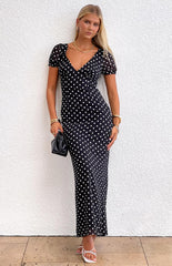 Blonde model wearing a black polka dot maxi dress with short puff sleeves and a v neckline paired with gold jewellery