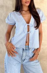 Close up of girl wearing a blue gingham tie up top, blue denim jeans and gold jewellery.