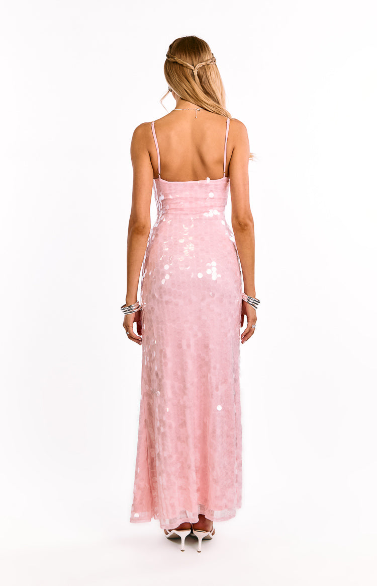 A girl shows the open back of a pink sequin maxi dress. This eye-catching evening gown features delicate criss-cross straps. A stunning choice for prom or a semi-formal event.