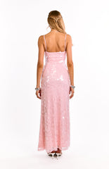 A girl shows the open back of a pink sequin maxi dress. This eye-catching evening gown features delicate criss-cross straps. A stunning choice for prom or a semi-formal event.