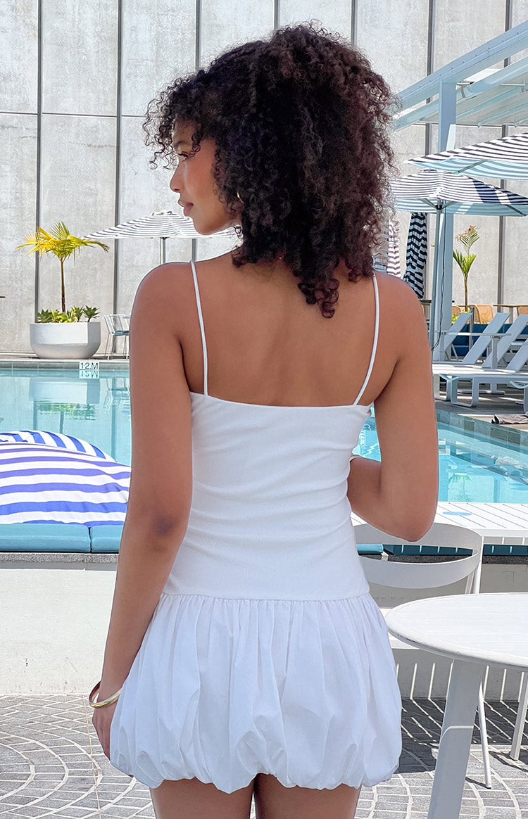 Girl facing away wearing white mini dress in front of pool area.