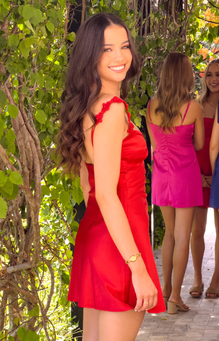 Girl looking over her shoulder in a red satin formal mini dress. This angle shows off the delicate floral appliqué on the straps and the dress's flattering- simple silhouette.