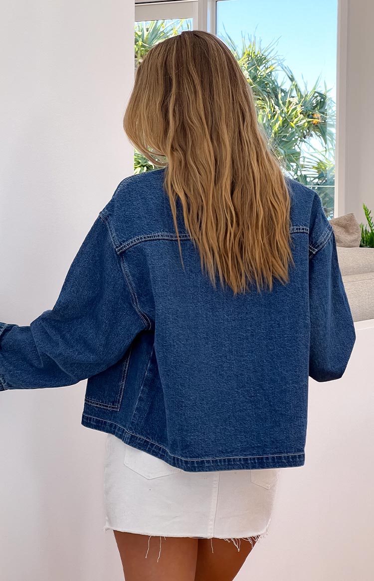 Back view of an oversized mid-wash denim jacket with visible contrast stitching- worn over a white mini skirt.