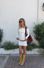 Model wearing a long-sleeve- white ribbed mini dress. The dress features a wide- off-the-shoulder neckline and is styled with a brown belt and tan boots.