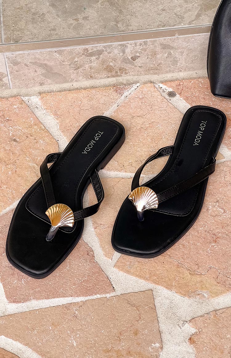 Two black flip-flops with gold and silver seashell embellishments are positioned on a light brown tiled surface. The brand "TOP MODA" is visible on the inner sole of each shoe.
