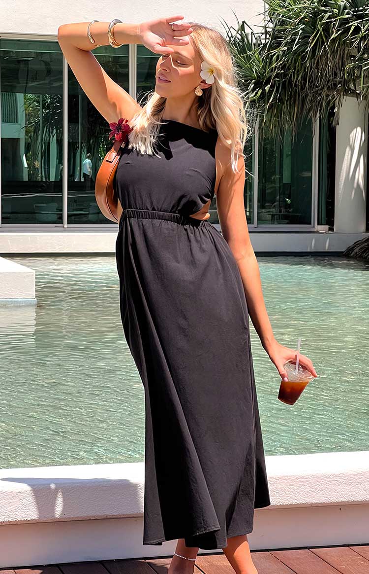 blonde model wears a black maxi dress with a flower in her hair holding a handbag