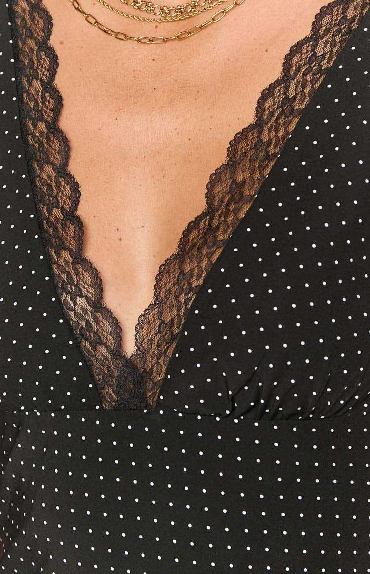 Model wearing a black mini dress with white polka dots and a black lace-trimmed V-neckline- accessorized with gold bangles.
