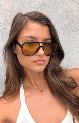 brunette model wearing black aviator frame sunglasses with yellow lenses