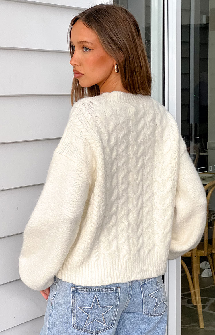 Rear view of our model wearing an off-white cable-knit cardigan with a slightly oversized fit and balloon sleeves.