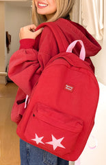 A front view of a red backpack with a zippered front pocket featuring two light pink star appliques.