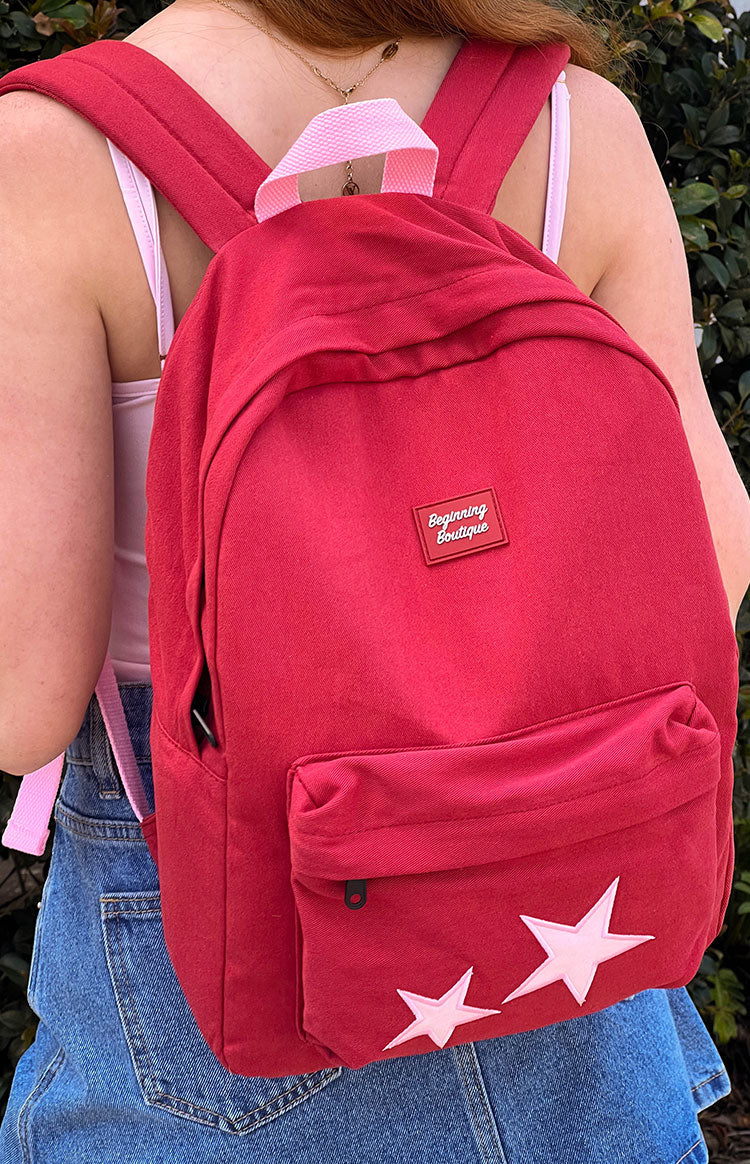 A red backpack with a front zippered pocket and two large white star appliques on the bottom.
