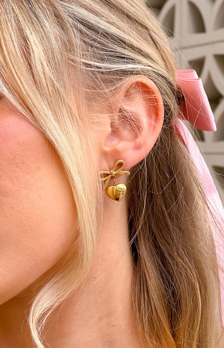 gold plated push back earrings with a bow detail and dangly heart