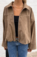 Close-up of a model wearing an open brown suede-like or corduroy jacket over a black ribbed top