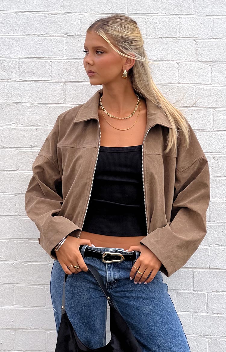 Close-up of a model wearing an open brown suede-like or corduroy jacket over a black ribbed top