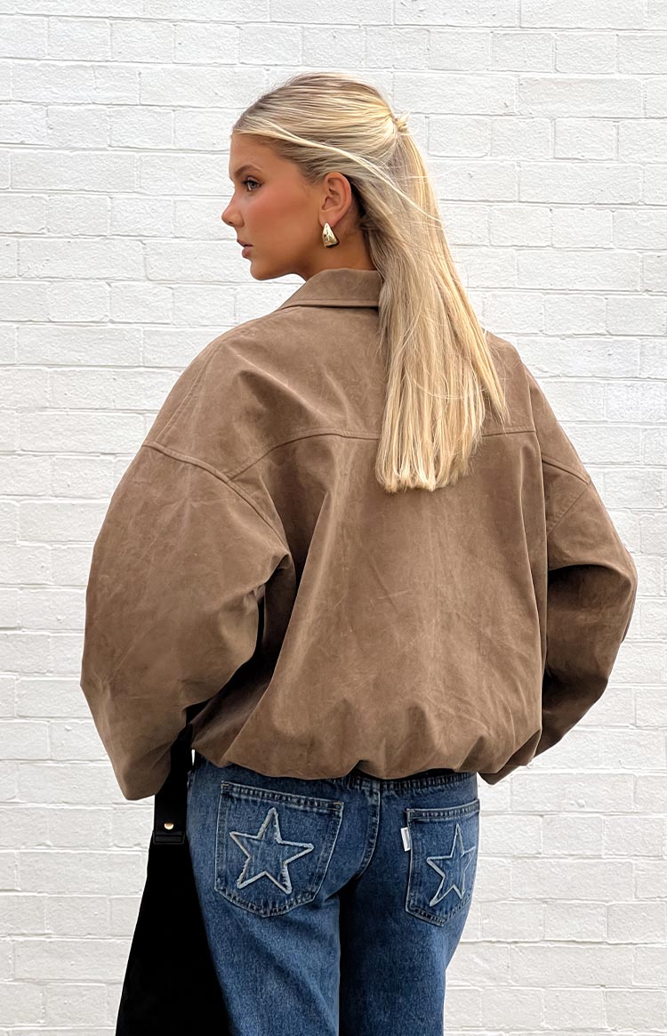 Close-up of a model wearing an open brown suede-like or corduroy jacket over a black ribbed top