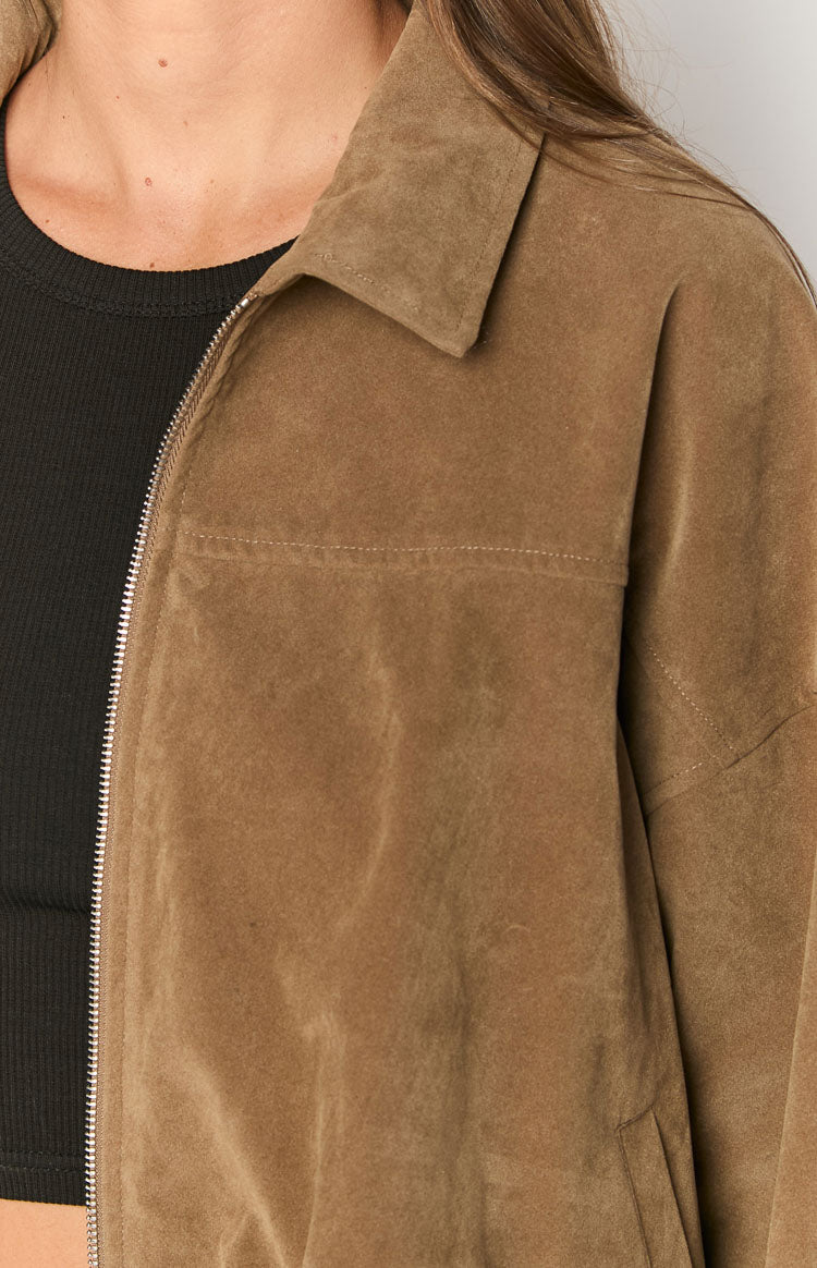 Close-up of a model wearing an open brown suede-like or corduroy jacket over a black ribbed top