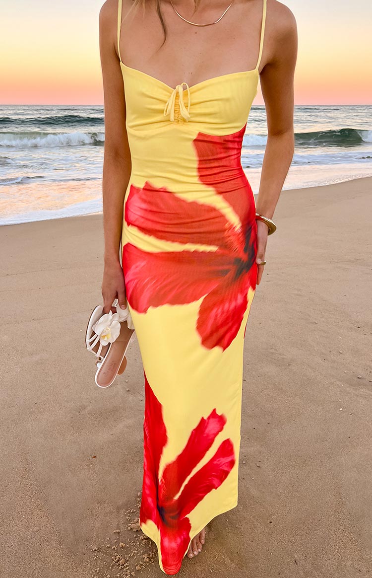A fitted yellow maxi dress with large- bold red hibiscus floral prints- featuring thin spaghetti straps and a ruched tie-front bust.