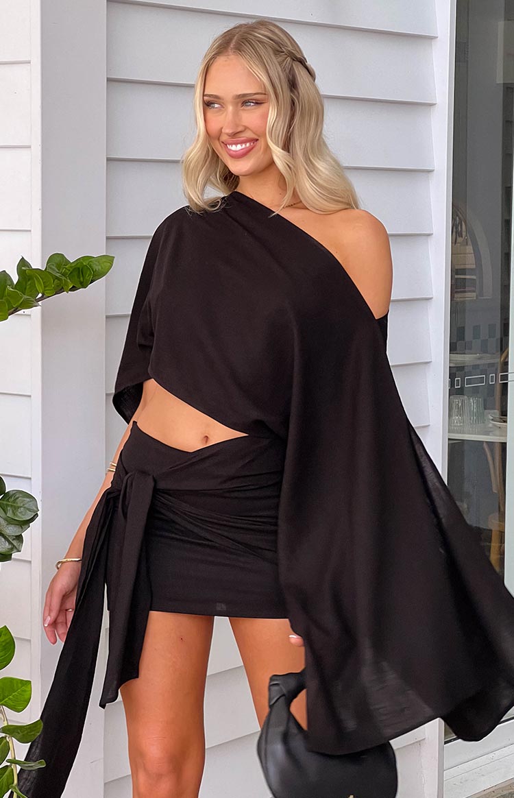 blonde model wearing black mini dress with draped arm detail and tie side skirt detail and small black bag