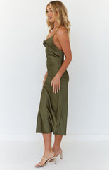 Blonde model wearing a khaki green, satin midi dress, while posing side-on to the camera in a white studio. 