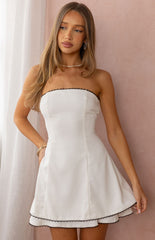 A female model wearing a white strapless mini dress with black scalloped lace trim along the neckline and hem.