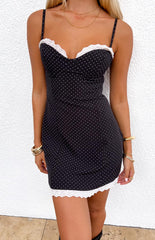 Girl wearing a black mini dress with a white polka dot pattern and lace trim at the bust and hem paired with gold jewellery