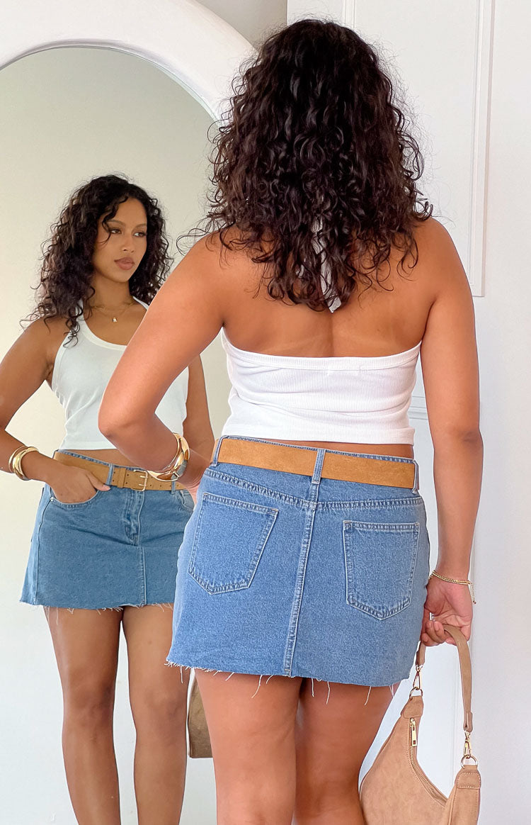 a gold starfish necklace and denim mini skirt holding a drink