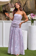 Brunette model wearing purple strapless maxi dress and holding a drink in front of white decorations.