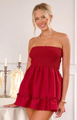 a red mini dress is worn by a blonde model with gold bracelets beside a table with candles