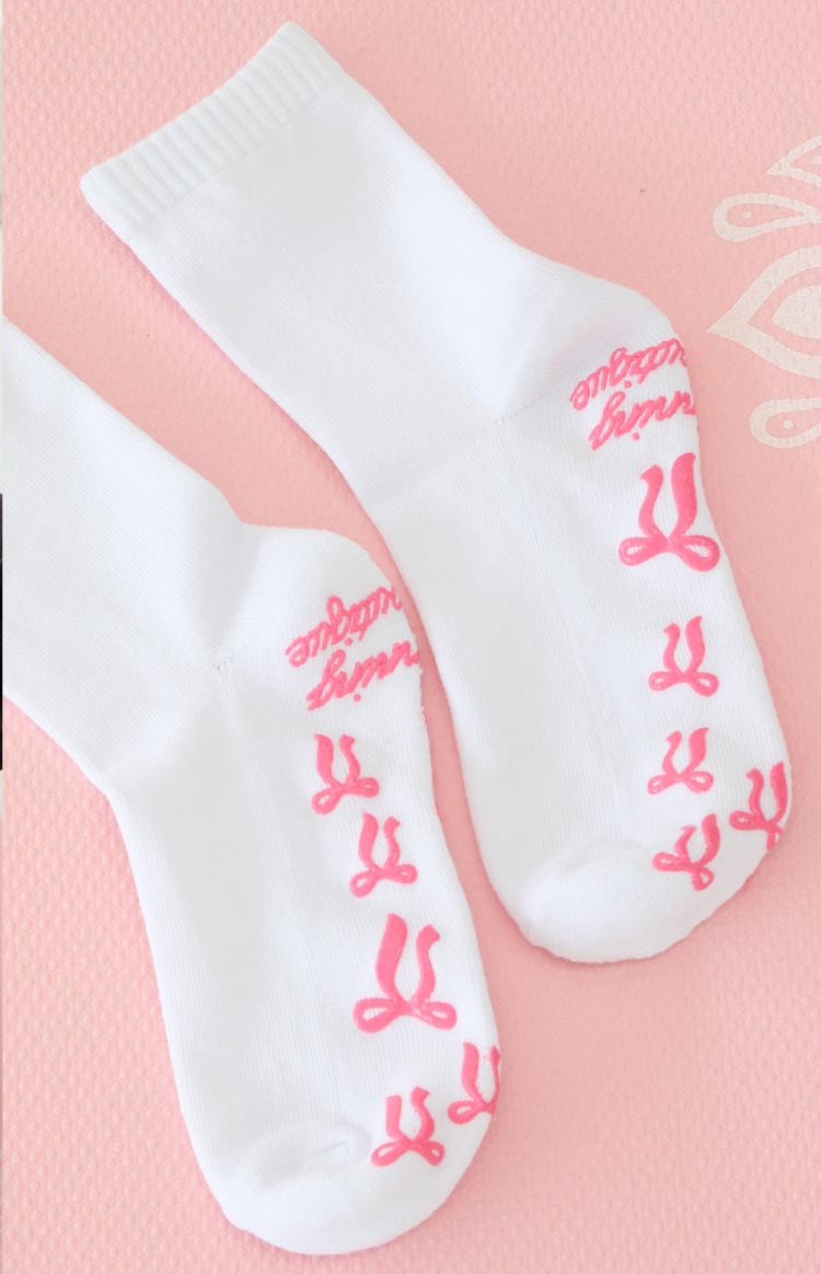 white yoga socks with pink bow shaped grips on the bottom and a graphic 'beginning boutique' grip
