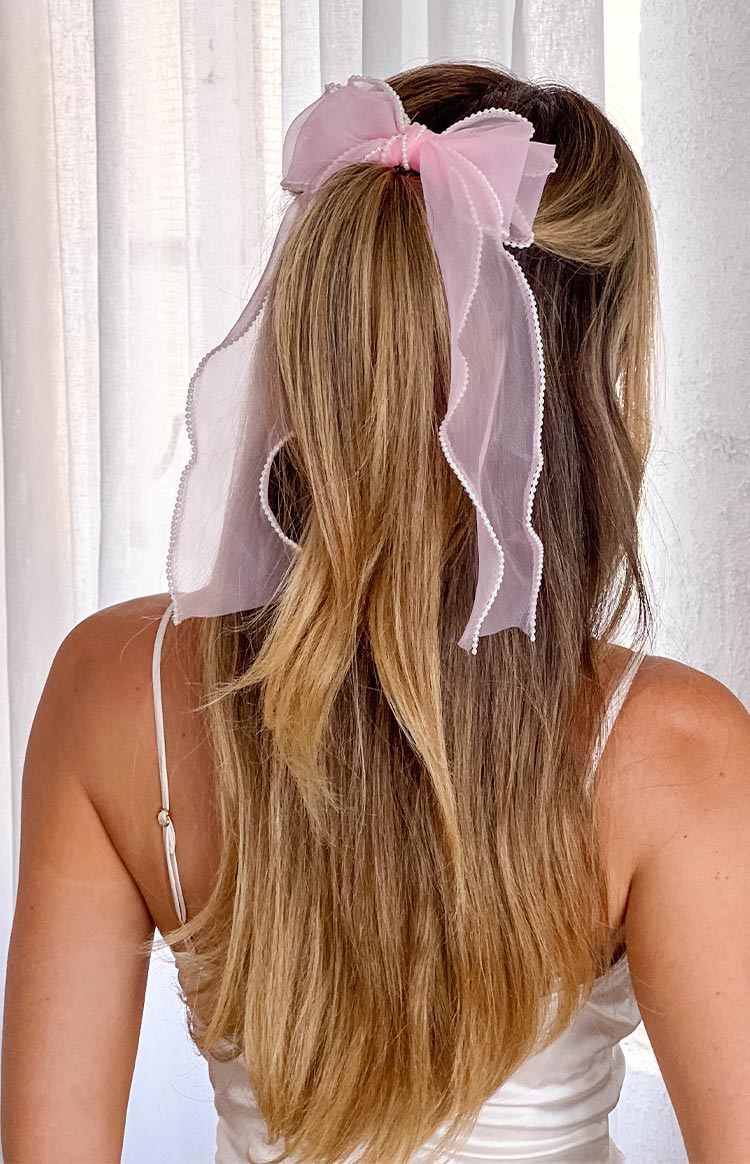 blonde model wearing a pink bow hair accessory with pearl details styled with a white top