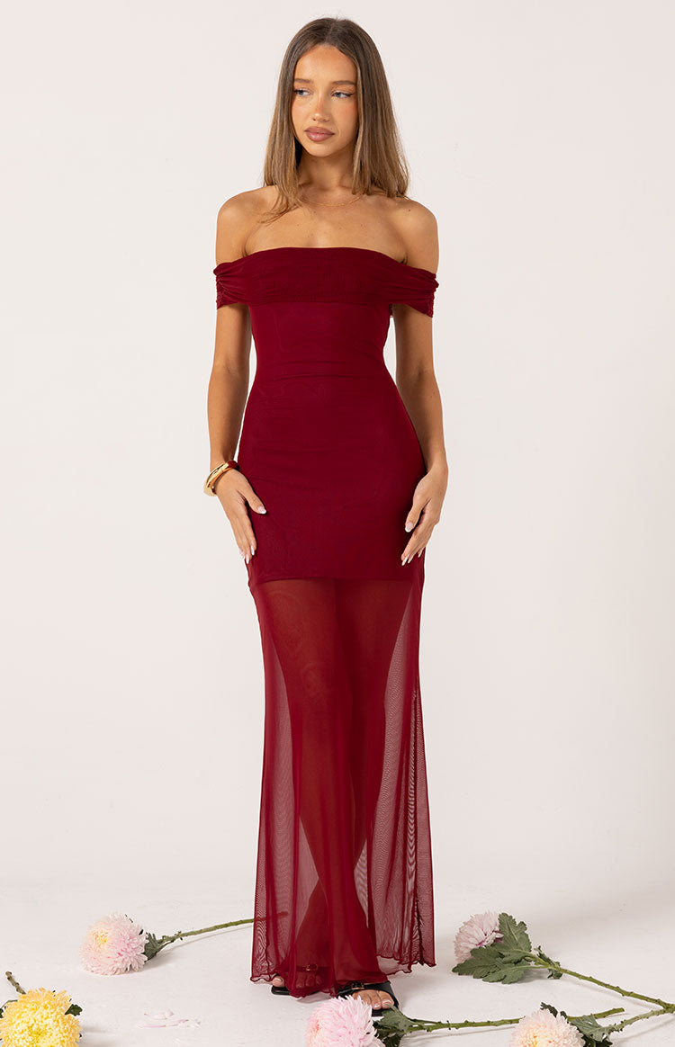 A full-body shot of a model wearing a deep red off-the-shoulder dress with a floor-length mesh overlay skirt.