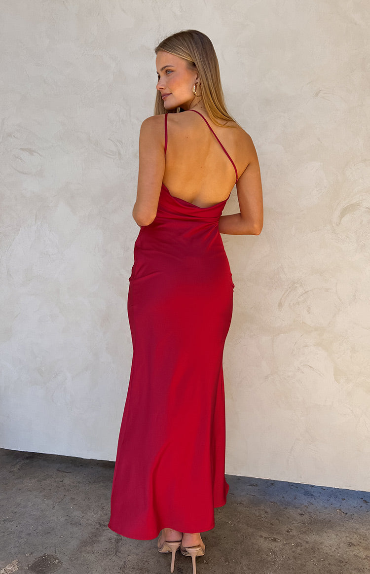 Girl facing towards white wall wearing red backless maxi dress and nude heels.