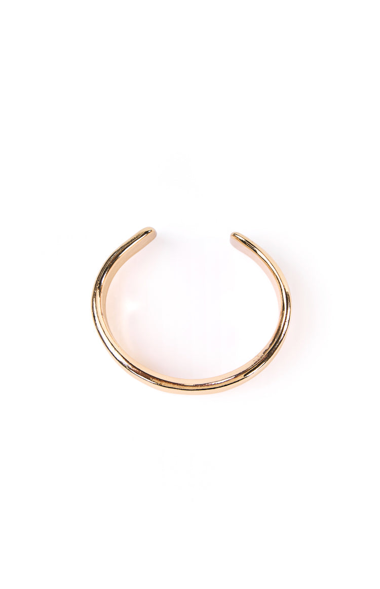 A model's wrist is shown with a wavy gold cuff bangle. This statement jewellery piece has an organic fluid shape. A perfect accessory for a party outfit or formal event.