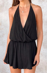 A close-up view of a black halter neck playsuit- featuring a deep V-neckline with a wrap-front bodice and an elasticated waist leading to relaxed shorts