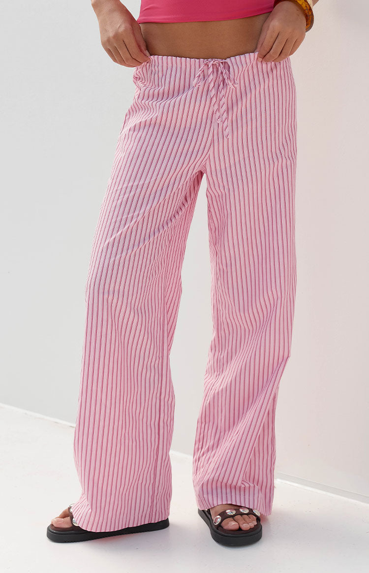 Full-length image of our model wearing a pair of pink and white striped pants with a drawstring waistband and a wide-leg fit.