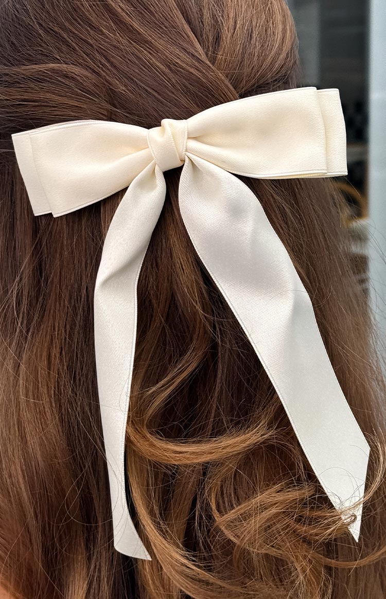A close-up of a cream satin bow hair clip with long tails