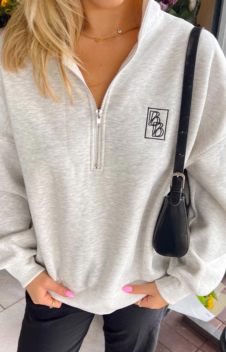 Close-up of a light grey marl quarter-zip jumper- highlighting the embroidered logo on the chest- a versatile casual top.